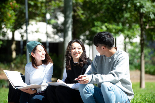 外でノートを広げて話している学生3人