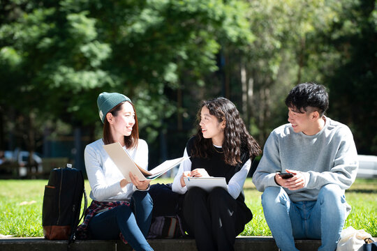 外でノートを広げて話している学生3人