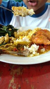 A boy from Indonesia eats balado chicken with gusto. Balado chicken is one of the menus of Padang rice besides rendang. Eating using bare hands without spoons. A unique eating habit in Indonesia