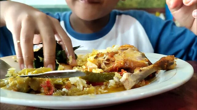 A boy from Indonesia eats balado chicken with gusto. Balado chicken is one of the menus of Padang rice besides rendang. Eating using bare hands without spoons. A unique eating habit in Indonesia