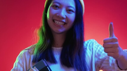 Education recommend. Study approval. Happy satisfied smiling woman student pointing at books showing thumb up like gesture in green blue neon light on red free space.