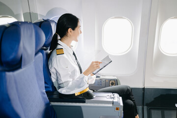 Asian Confident Feale pilot in uniform leaning at the passenger seat while standing inside of the...