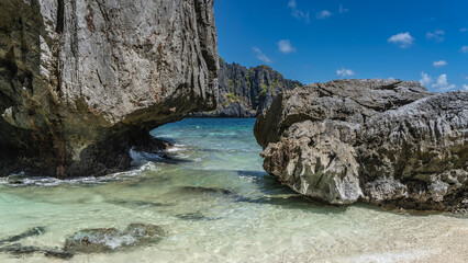 Picturesque karst rocks in the ocean near the shore. Steep rough furrowed slopes. The sandy bottom is visible through the clear turquoise water. Philippines. Palawan. Bacuit Bay.