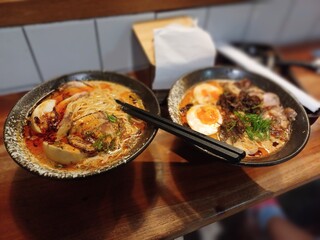 Two Bowls of Ramen Noodles with Boiled Eggs, Spicy Broth and a Pair of Chopsticks in One of the Bowls