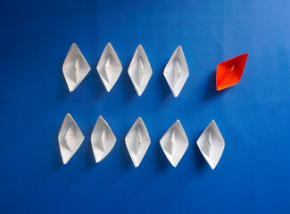 Being Different Concept. Red Paper Ship Among White Paper Boats On Blue Background