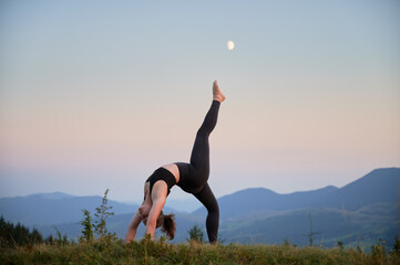 Woman practicing yoga outdoors in the mountains in a serene, natural setting. Female performing...
