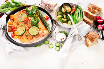 Grilled salmon and vegetables on wooden light background. Dinner table with cooked fish, tomatoes, asparagus