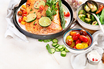 Grilled salmon and vegetables on wooden light background. Dinner table with cooked fish, tomatoes, asparagus