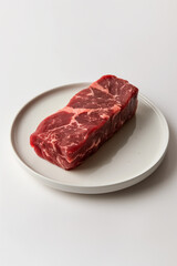 The raw beef steak rests on a round white plate with a minimal design, ready to be cooked.