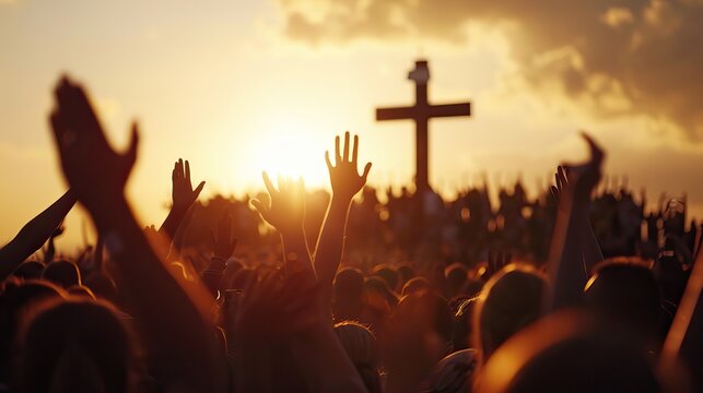 A large group of people raising hands in praise with a cross and sunset in the background