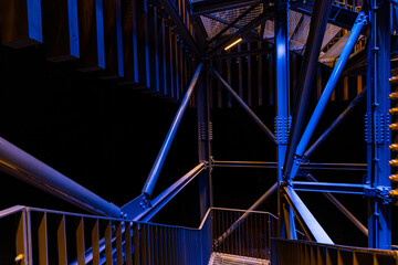 A close-up, abstract view of metal beams and structures illuminated with blue and yellow lights....