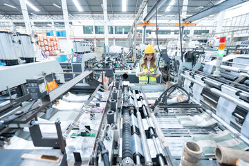 A long-haired European female engineer is working in a large industrial plant with machinery that is producing materials such as steel and plastic for export to all continents of the world.