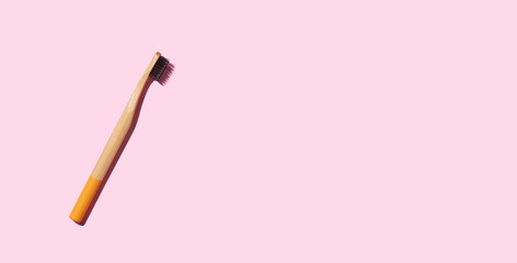 Bamboo toothbrush on pink background with copy space.