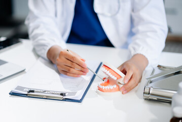 Fototapeta premium Dentist sitting at table with jaw samples tooth model and working with tablet and laptop. professional dental clinic.
