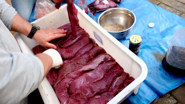 Spicing kudu game meat pieces in container for curing to make biltong jerky