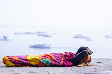 Portrait of old holy sadhu baba in traditional dress sleeping on the ghats near ganges in varanasi.