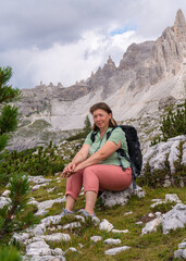 Happy middle aged woman enjoying  beautiful view of high cliffs. Sitting on  rock. Healthy lifestyle concept, hiking, tourism.  Dolomite Alps, South Tyrol, Italy