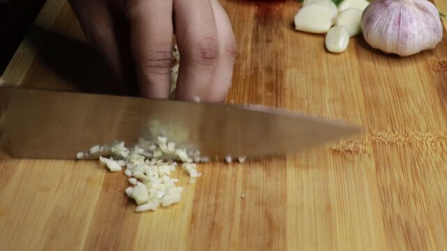 Close up shot of knife dicing the garlic cloves to small pieces. Concept of preparing healthy meals. Knife Grinds Clove Of Garlic. Ingredients For Cooking In The Kitchen. Dinner Dish Cooking. 