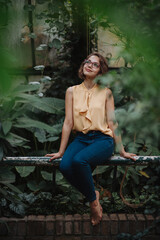 Beautiful woman sitting in botanical garden, in the middle of lush green foliage, meditating, connecting with nature.