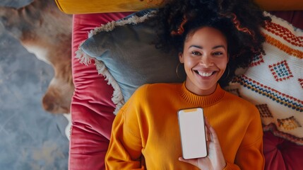 A cozy scene of woman lying on a comfortable couch wearing a bright orange sweater while holding a smartphone, surrounded by colorful cushions and a relaxed atmosphere, perfect for unwinding.
