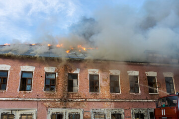 Flames and smoke billow from a historic brick structure as firefighters work tirelessly to extinguish the fire during the twilight hours.