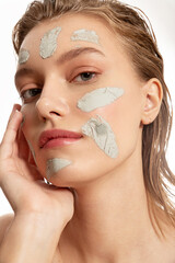 Close up of  woman face  with  strokes of clay mask on her face .