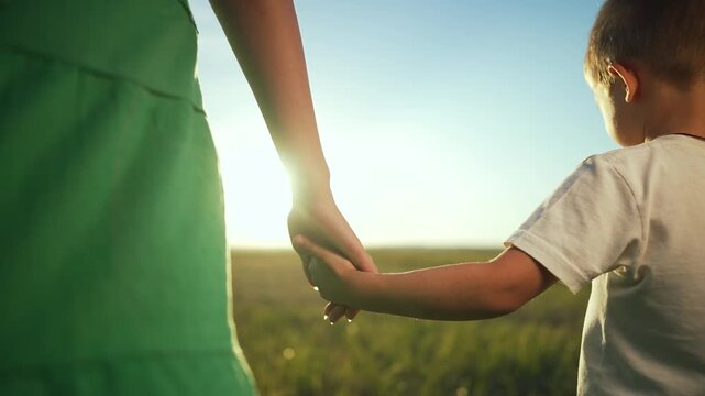 Happy Family hand in hand in park. Happy Mother and son enjoy sunset together. Dreamy family bond outdoors. Hands of family together in park. Concept of unity and love. Mother and son walking together