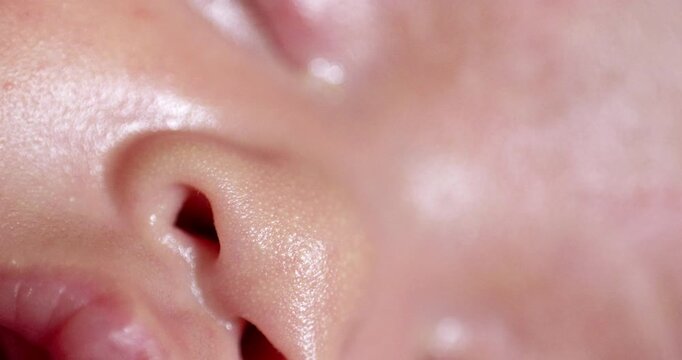 A close-up shot of a sleeping newborn infant's nose, lips and closed eyes, while showing its reddish skin.