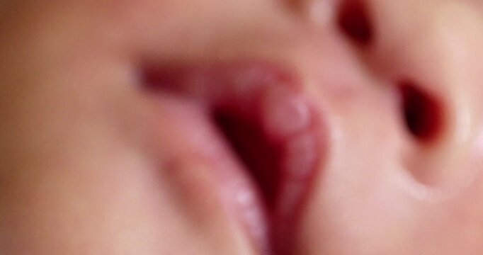 Blurry close-up shot of a newborn infant while showing its reddish skin, pinkish lips and the holes of its nostrils.