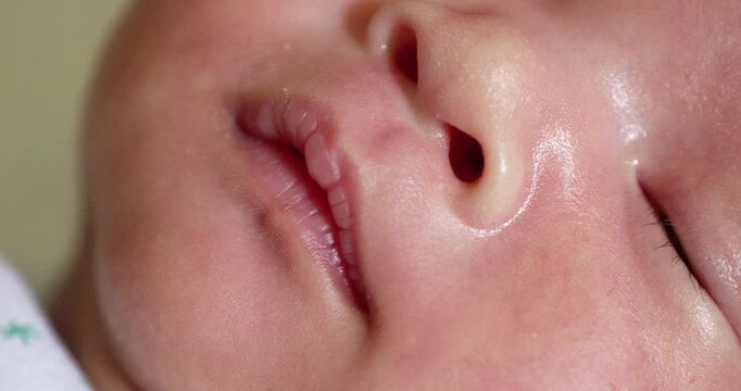A close-up portrait shot of a sleeping baby while it is slightly opening its mouth and pursing its lips in its sleep.