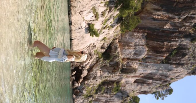 Pregnant blonde woman in shallows of Nugal Beach near coastal cliff, vertical