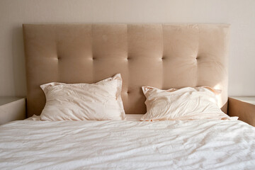 Beige tufted headboard with pillows and bedding in a cozy bedroom. Comfort and relaxation concept.