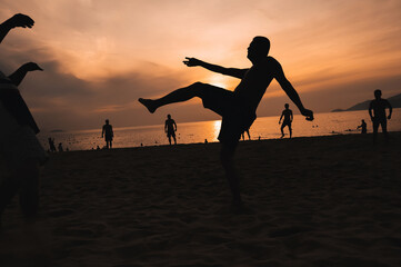 Silhouettes of Asian men playing beach football on beach by the sea at sunset