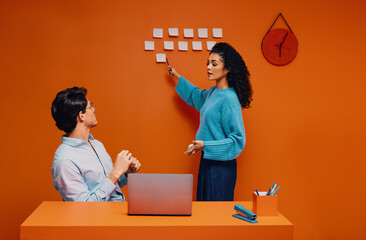 Woman instructing a colleague on strategy planning using sticky notes during a meeting in a monochromatic agency office