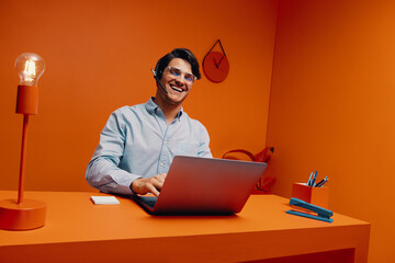 Male support agent with eyeglasses and headset working with laptop in bright office