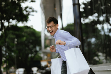 A cheerful young man walking outside a trendy store, carrying multiple shopping bags, exuding happiness and style during a fun shopping spree in the city.