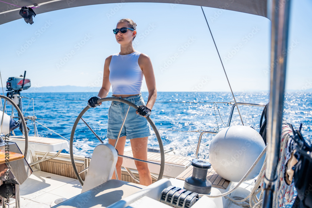 Wall mural young woman female captain stands at the helm and controls a sailboat during a journey by sea