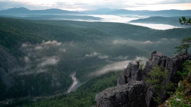 Scenery morning clouds at Ural mountains. Fog enveloping a mountain valley at sunrise from a high point, shifting from darkness to radiant light. Golden hour