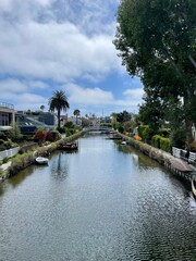Fototapeta premium Ruhige Atmosphäre bei den Venice Canals in Los Angeles. Mehrere Wolken in blauem Himmel, Bäume und Palmen am Rande des Kanals.
