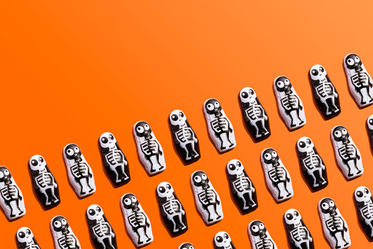 Pattern of rows of Halloween candy with skeleton wrapping against orange background