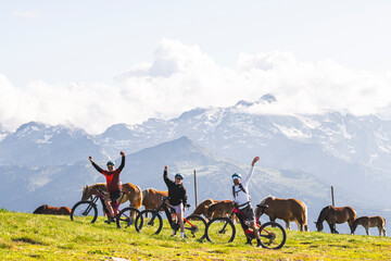 Friends waving hands and standing with bicycle amidst horses on mountain