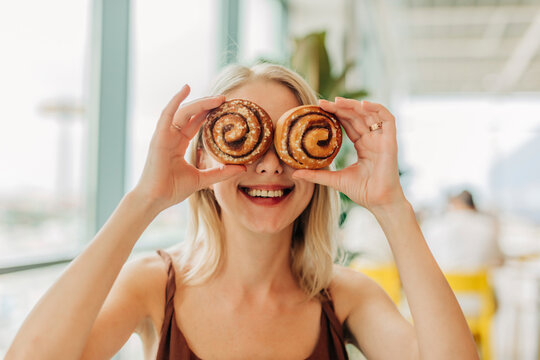 Woman covering eyes with cinnamon buns in cafe