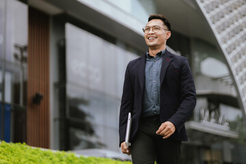 A determined young businessman in a city, confidently working on his laptop outdoors, dressed in a...