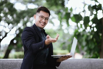 A determined young businessman in a city, confidently working on his laptop outdoors, dressed in a...