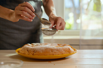Hands of woman sifting powdered sugar on apple pie