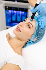 A cosmetologist wearing gloves performs vacuum cleaning and polishing of the facial skin of a middle-aged woman in a cosmetology clinic. Professional moisturizing and rejuvenating hardware procedures.