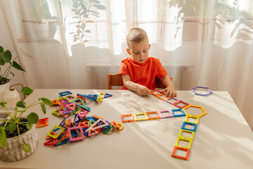 Boy arranging magnetic toy blocks on table at home