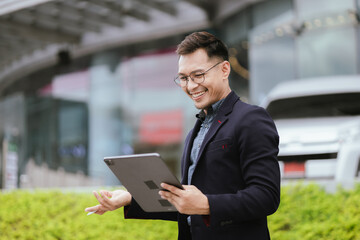 Fototapeta premium A cheerful young Asian businesswoman in a modern city, smiling confidently while using her smartphone outdoors, dressed in a professional suit, embodying success and digital connectivity.