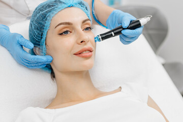 A cosmetologist wearing gloves performs vacuum cleaning and polishing of the facial skin of a...