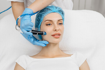 A cosmetologist wearing gloves performs vacuum cleaning and polishing of the facial skin of a...